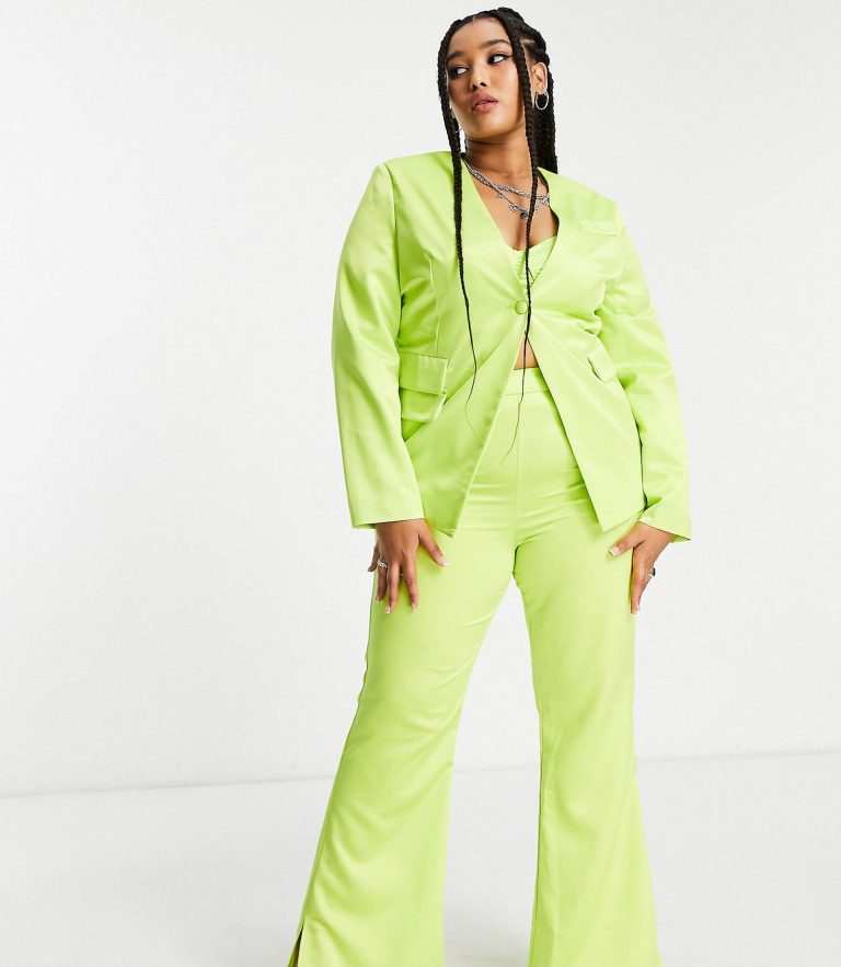 Femme portant un tailleur vert fluo composé d'une veste cintrée et d’un pantalon évasé, posant avec assurance sur fond blanc.