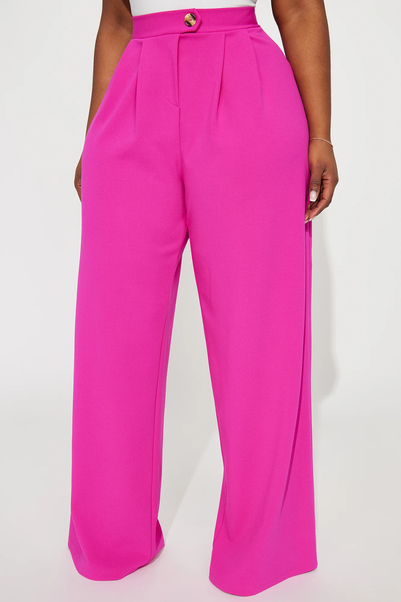 Une femme porte le pantalon fuchsia nommé Maya, confectionné en crêpe de soie mélangé (70 % soie et 30 % laine vierge). Ce pantalon à taille haute est accentué par un bouton doré et des plis marqués à l’avant, offrant une allure sophistiquée.