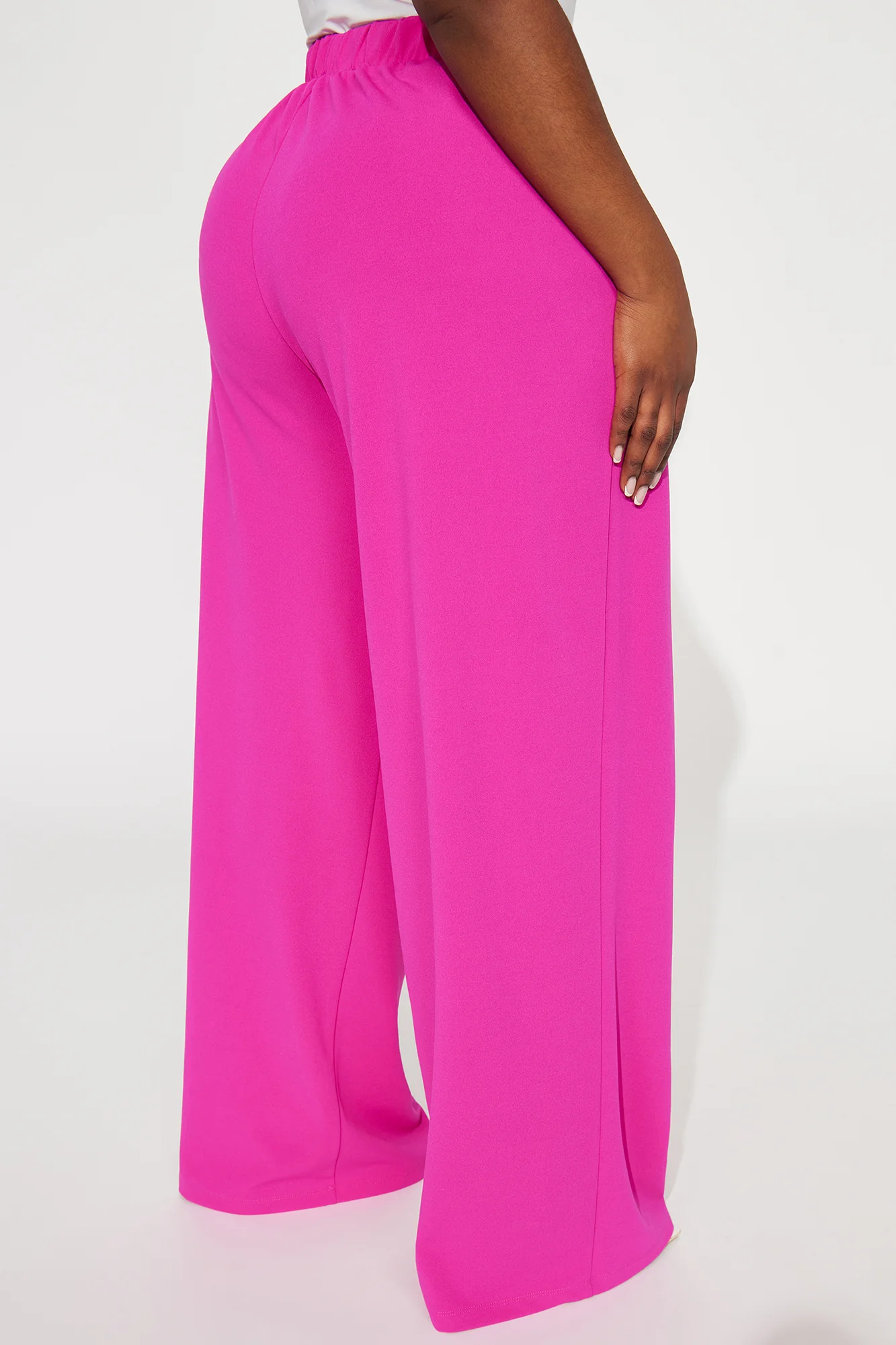 Une femme porte le pantalon fuchsia nommé Maya, confectionné en crêpe de soie mélangé (70 % soie et 30 % laine vierge). Ce pantalon à taille haute est accentué par un bouton doré et des plis marqués à l’avant, offrant une allure sophistiquée.