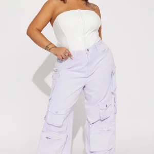 Une femme porte le pantalon cargo lavande nommé Gaëlle, confectionné en gabardine de coton. Ce pantalon large est doté de multiples poches fonctionnelles et d’une teinte pastel douce. Elle l’associe à un corset blanc structuré et des talons pointus, créant un look audacieux et féminin.