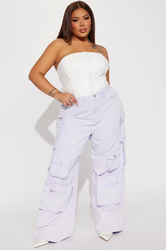 Une femme porte le pantalon cargo lavande nommé Gaëlle, confectionné en gabardine de coton. Ce pantalon large est doté de multiples poches fonctionnelles et d’une teinte pastel douce. Elle l’associe à un corset blanc structuré et des talons pointus, créant un look audacieux et féminin.