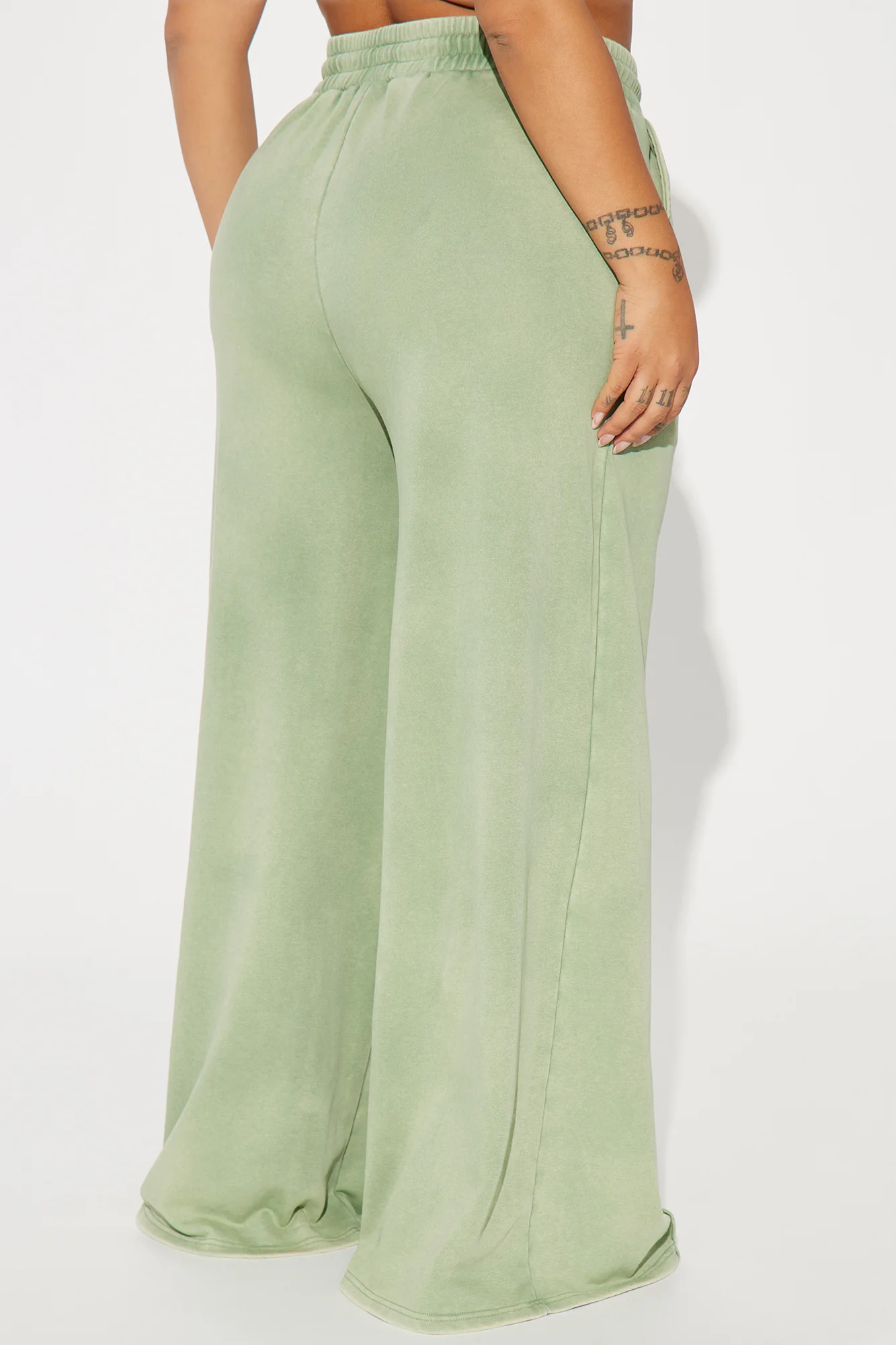Une femme porte le pantalon large vert nommé Julie, confectionné en molleton de coton. Ce pantalon fluide est doté de coutures apparentes et d’une taille élastique avec cordon.