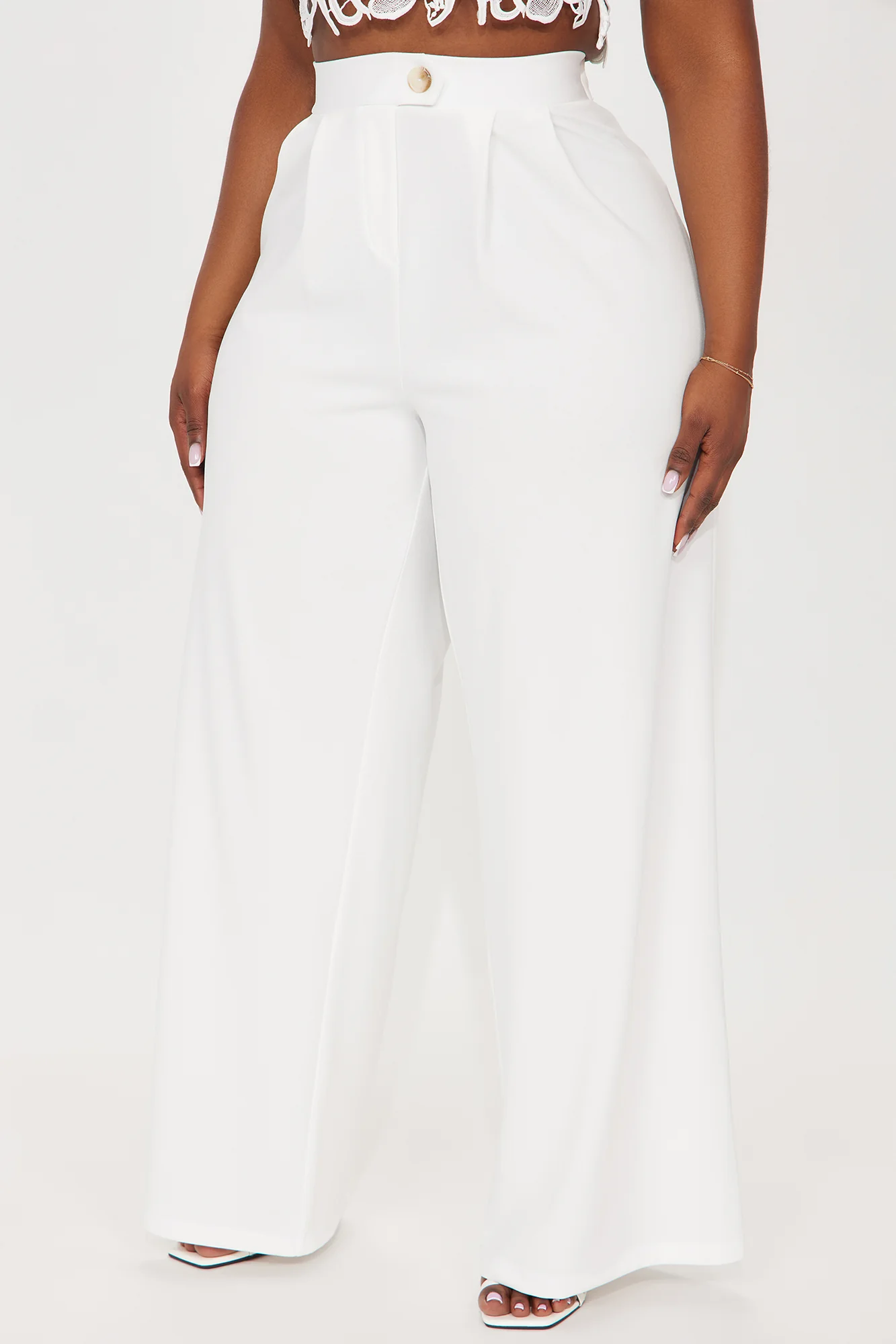 Une femme porte le pantalon blanc nommé Sandra, confectionné en crêpe de laine. Un pantalon à taille haute, orné d’un bouton doré et doté d’une coupe large.
