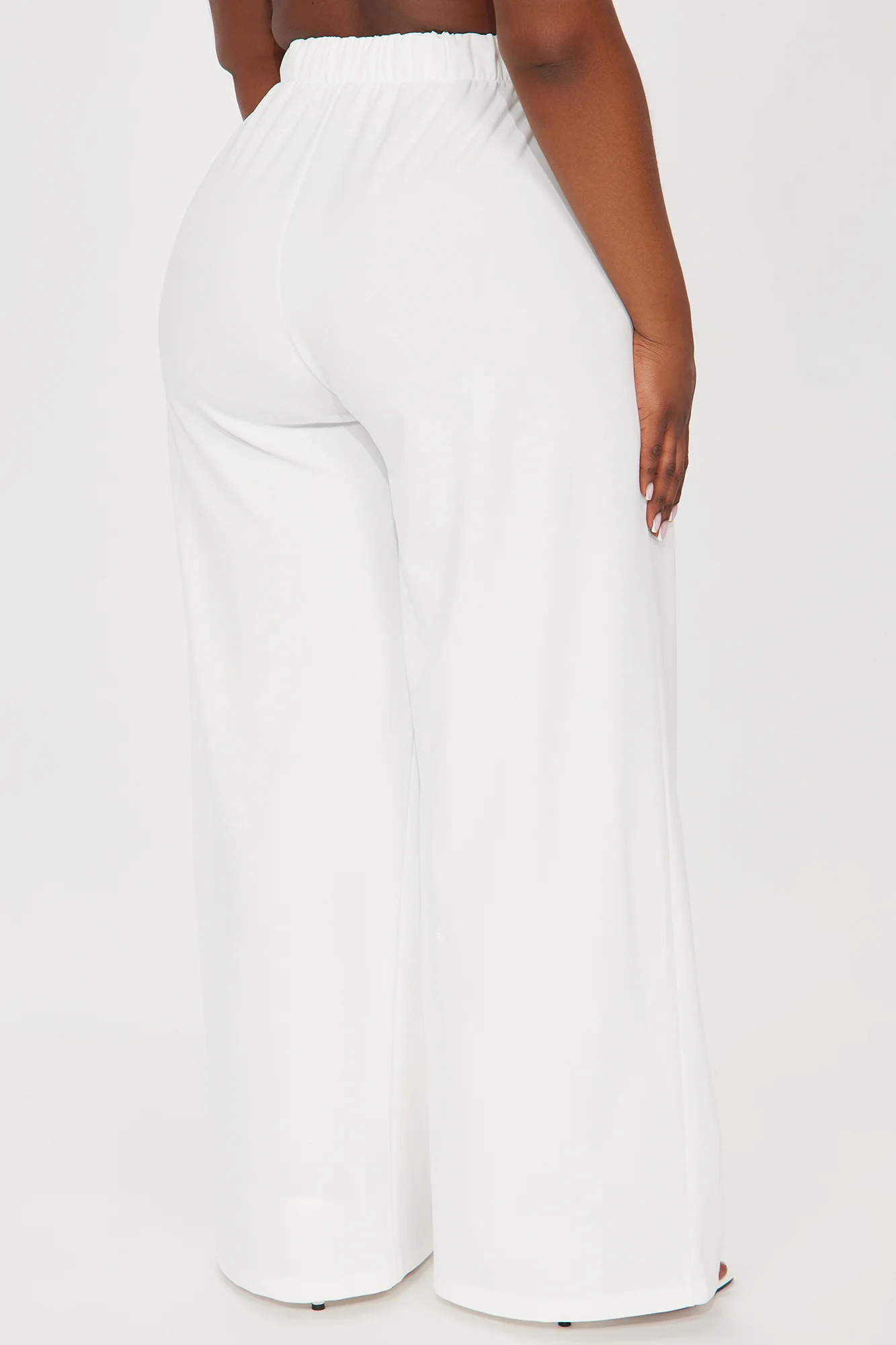 Une femme porte le pantalon blanc nommé Sandra, confectionné en crêpe de laine. Un pantalon à taille haute, orné d’un bouton doré et doté d’une coupe large.