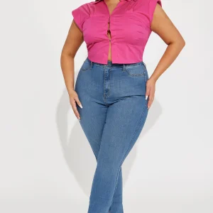 Une femme curvy porte un top rose vif en coton satiné, avec un col chemise structuré et une coupe ajustée qui met en valeur sa silhouette. Le top est légèrement ouvert à l'avant pour une touche sensuelle. Elle l'associe à un jean skinny bleu et des talons transparents, créant un look moderne et chic.
