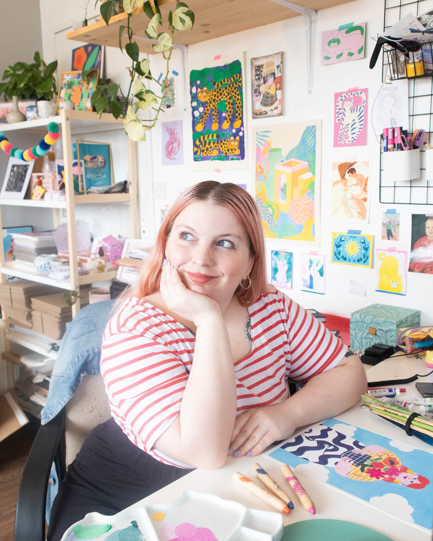 Marie Boiseau dans son atelier, entourée de ses illustrations colorées, assise à son bureau avec des crayons et une palette de peinture