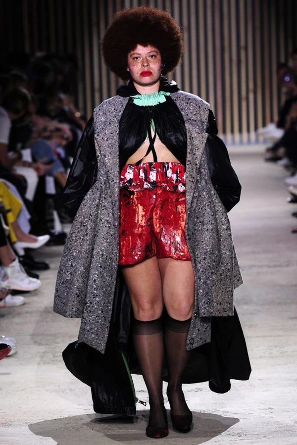 Odile Gautreau défile pour Ester Manas en 2018, tenue colorée, manteau large, coiffure afro marquante, attitude assurée.
